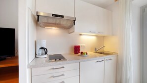 A modern kitchen with white cabinets, a stainless steel range hood, a coffee maker, a fruit bowl, and a sink.