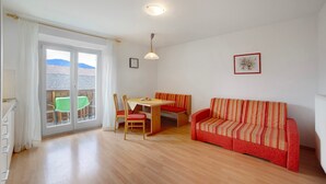 A room with a wooden floor, a red sofa, a dining table with chairs, and a window with a view of buildings.