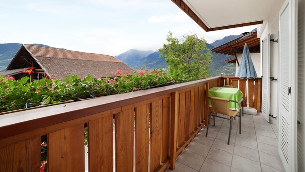 A balcony with a wooden railing, a table with a green tablecloth, and a chair.
