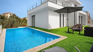 Uma casa moderna com piscina, móveis de exterior e céu claro.