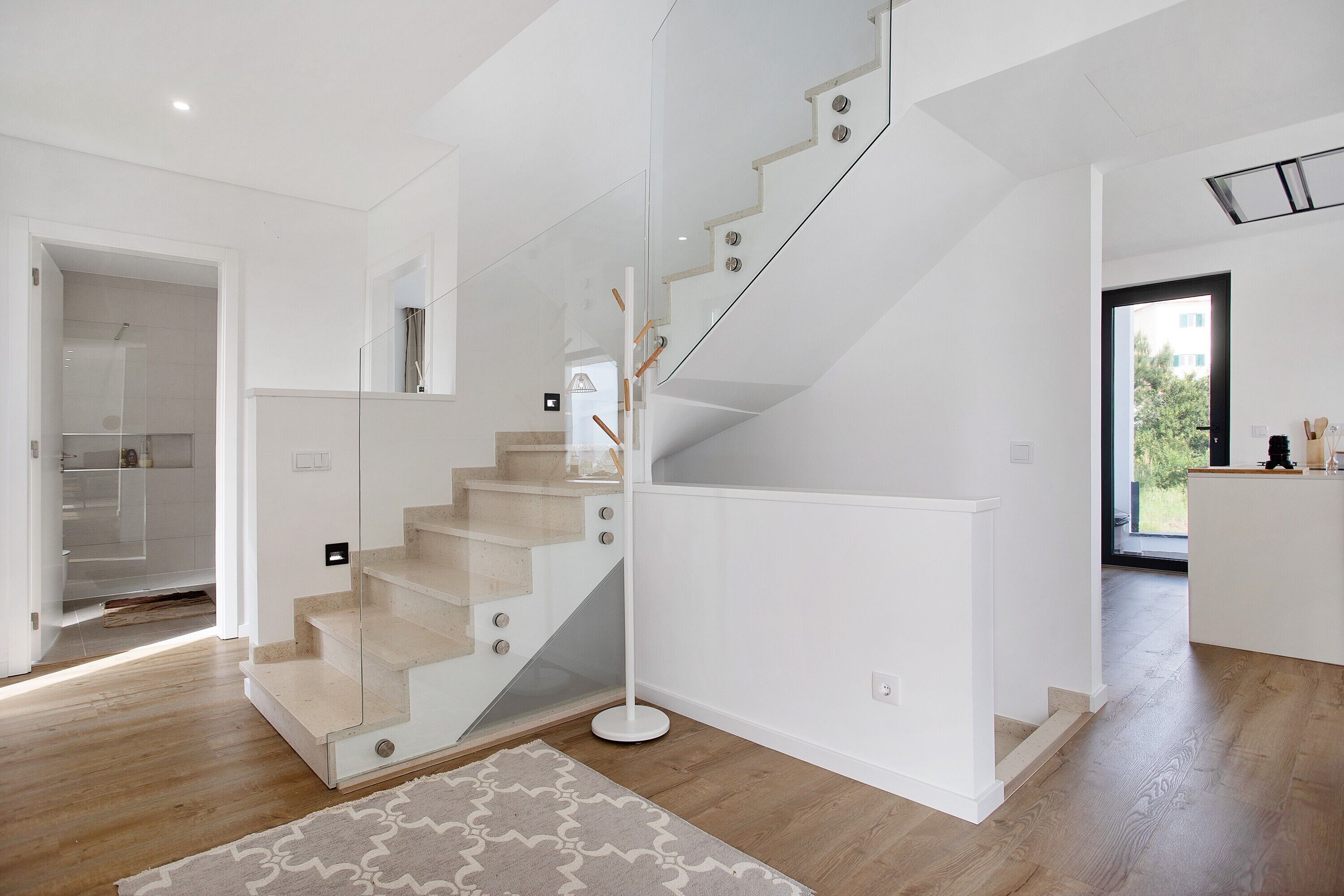 Ein modernes Interieur mit einer Treppe, einer Küchenzeile und Blick durch eine Glastür.