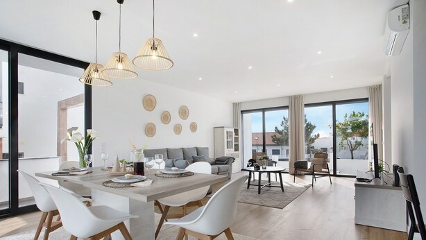 Uma zona de refeições moderna com uma mesa comprida, cadeiras brancas e luminárias pendentes.