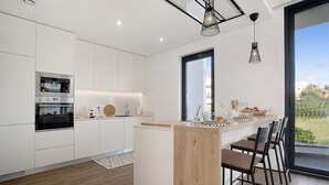 Cozinha moderna com armários brancos, uma ilha de madeira e uma janela ampla.