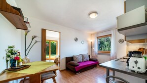 Un espacio habitable compacto con una mesa de comedor, un sofá, una kitchenette y vistas a zonas verdes a través de la puerta.