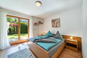Une chambre à coucher comprenant un lit, des tables de chevet, une commode, une fenêtre avec des rideaux, un tableau au mur et une vue sur un jardin.