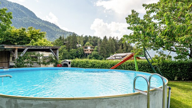 Una piscina al aire libre con escalera, rodeada de vegetación y montañas al fondo.