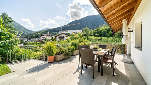 Una terrazza con tavolo e sedie, piante in vaso e vista su una città e montagne.