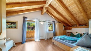 Una stanza con soffitto in legno, un letto con coperta blu e verde, una scrivania in legno e una finestra con tende.