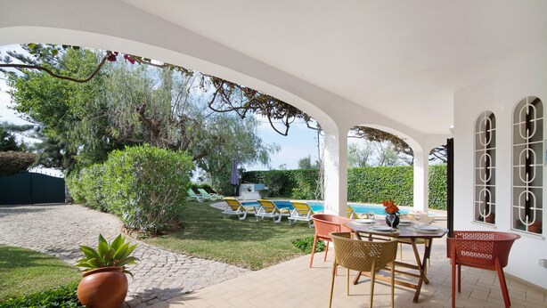 Eine überdachte Terrasse mit Pool, Gartenmöbeln und Blick auf den Poolbereich.