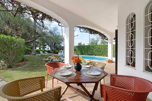 An outdoor patio with a table set for dining, surrounded by chairs, and a view of a swimming pool.