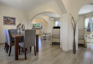 Uma sala de estar espaçosa com mesa de jantar, cadeiras, sofás e uma TV.