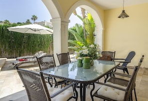 Un patio al aire libre con una mesa de vidrio, sillas de mimbre y un paraguas blanco.