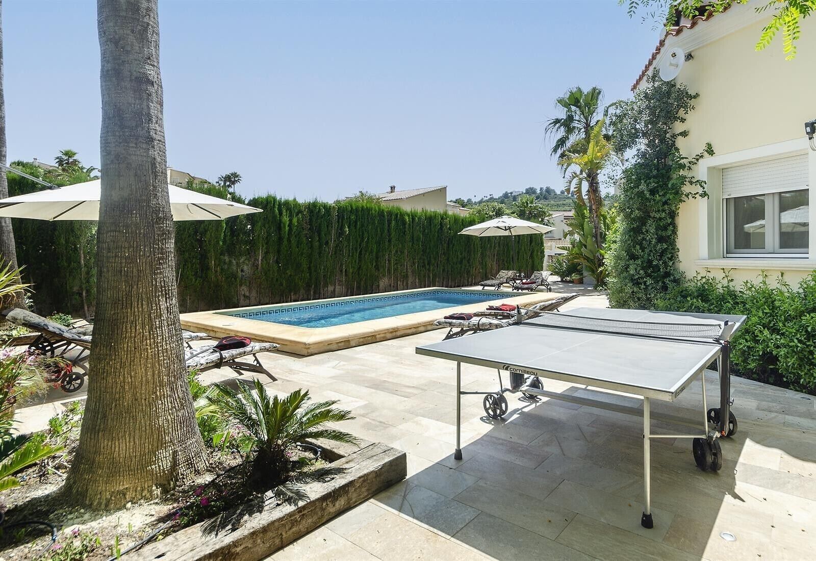 Un área de piscina con mesa de tenis, sillas de descanso y una piscina pequeña.