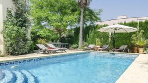 Ein Swimmingpool mit Liegestühlen und einem Sonnenschirm, umgeben von viel Grün.