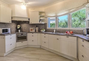 Una cocina con armarios blancos, microondas, horno, fregadero y ventana con vista a zonas verdes.