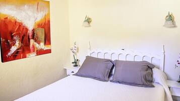 A bed with white headboard, two pillows, a nightstand with a lamp, and a painting on the wall.