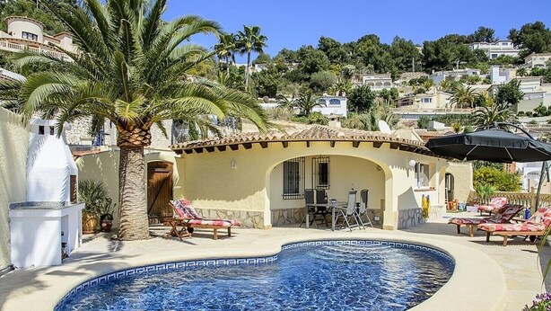 A pool with lounge chairs, a palm tree, and a building with a tiled roof. - Villa 'La Vista' with Sea View, Wi-Fi and Air Conditioning (Moraira)