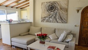 A living room with a beige sofa, a coffee table with magazines, a vase with red flowers, and a large abstract painting on the wall. - Villa 'La Vista' with Sea View, Wi-Fi and Air Conditioning (Moraira)