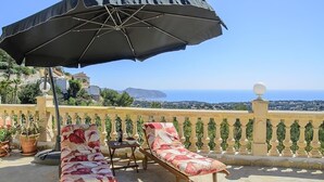 A terrace with two lounge chairs, a table, and an umbrella. The terrace overlooks a scenic view of the sea and a distant island. - Villa 'La Vista' with Sea View, Wi-Fi and Air Conditioning (Moraira)