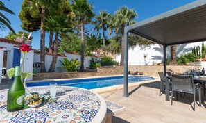 Zona junto a la piscina con una mesa de azulejos, una botella y un vaso de agua.