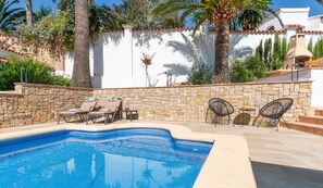 Una piscina con sillas de descanso y una pared de piedra.