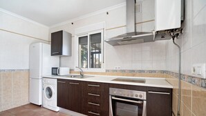 Une cuisine compacte équipée d’un lave-linge, d’un four, d’un micro-ondes et d’une fenêtre avec des stores.