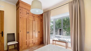 Une chambre dotée d’une grande armoire, d’un banc, d’un lit et offrant une vue sur l’extérieur par une fenêtre.