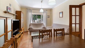 Un salon avec un téléviseur, des meubles en bois, une table à manger et une fenêtre avec des rideaux.