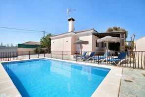 A swimming pool with lounge chairs, a covered seating area, and a building with a chimney.