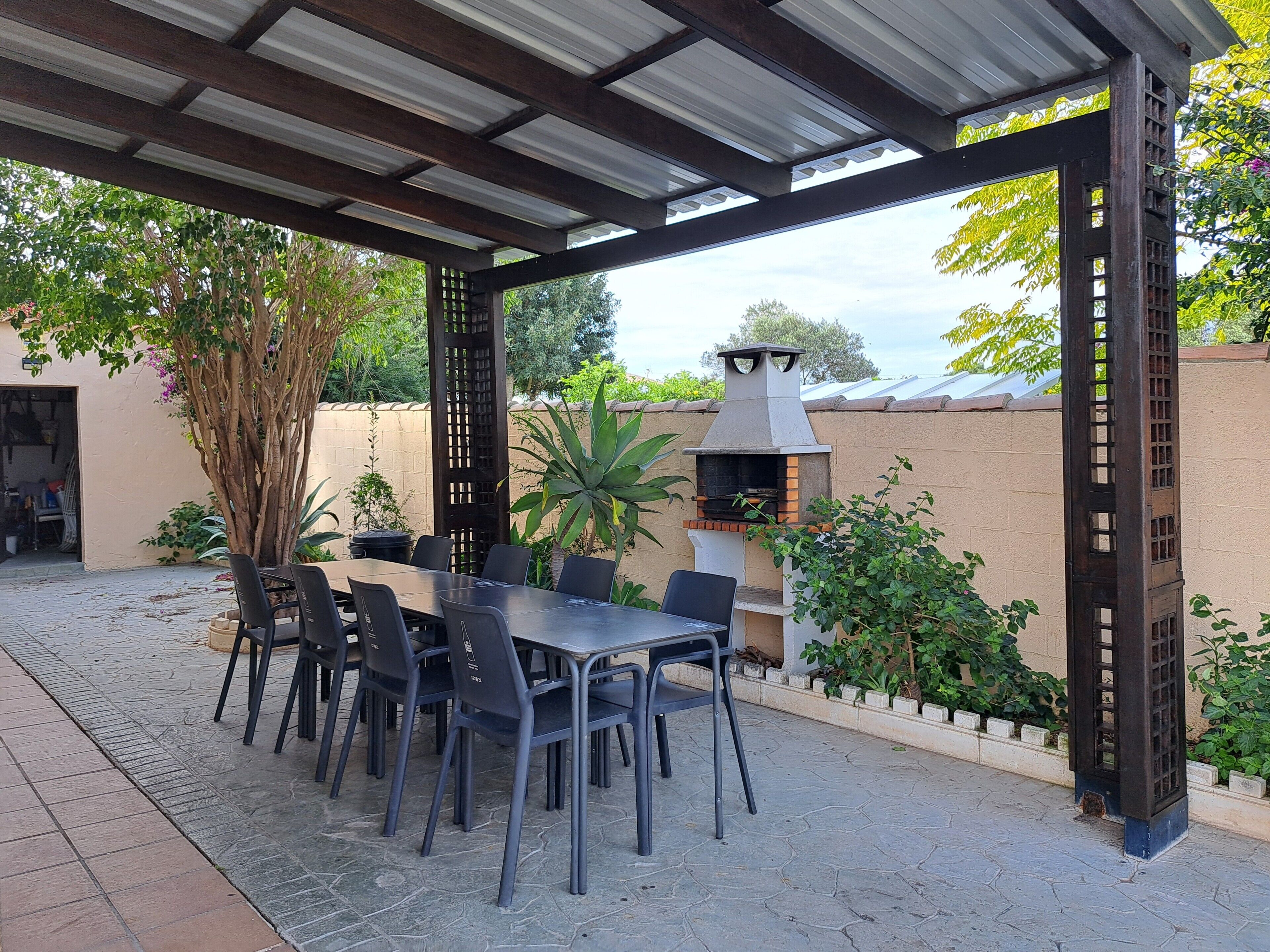 An outdoor patio with a covered seating area, a grill, and potted plants.