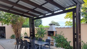 Une terrasse extérieure dotée d’un espace salon couvert, d’un barbecue et de plantes en pot.