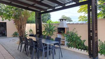 An outdoor patio with a covered seating area, a grill, and potted plants.