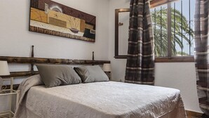 A bedroom with a bed, a nightstand, a lamp, a painting on the wall, and a window with curtains. - Holiday Home "Vista Bahia" with Sea Views, Private Pool and Wi-Fi (Moraira)