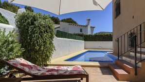A poolside area with a lounge chair, a white umbrella, and a staircase leading to a building. - Holiday Home "Vista Bahia" with Sea Views, Private Pool and Wi-Fi (Moraira)