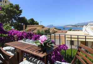 Un balcon avec une table, des chaises et des fleurs violettes.