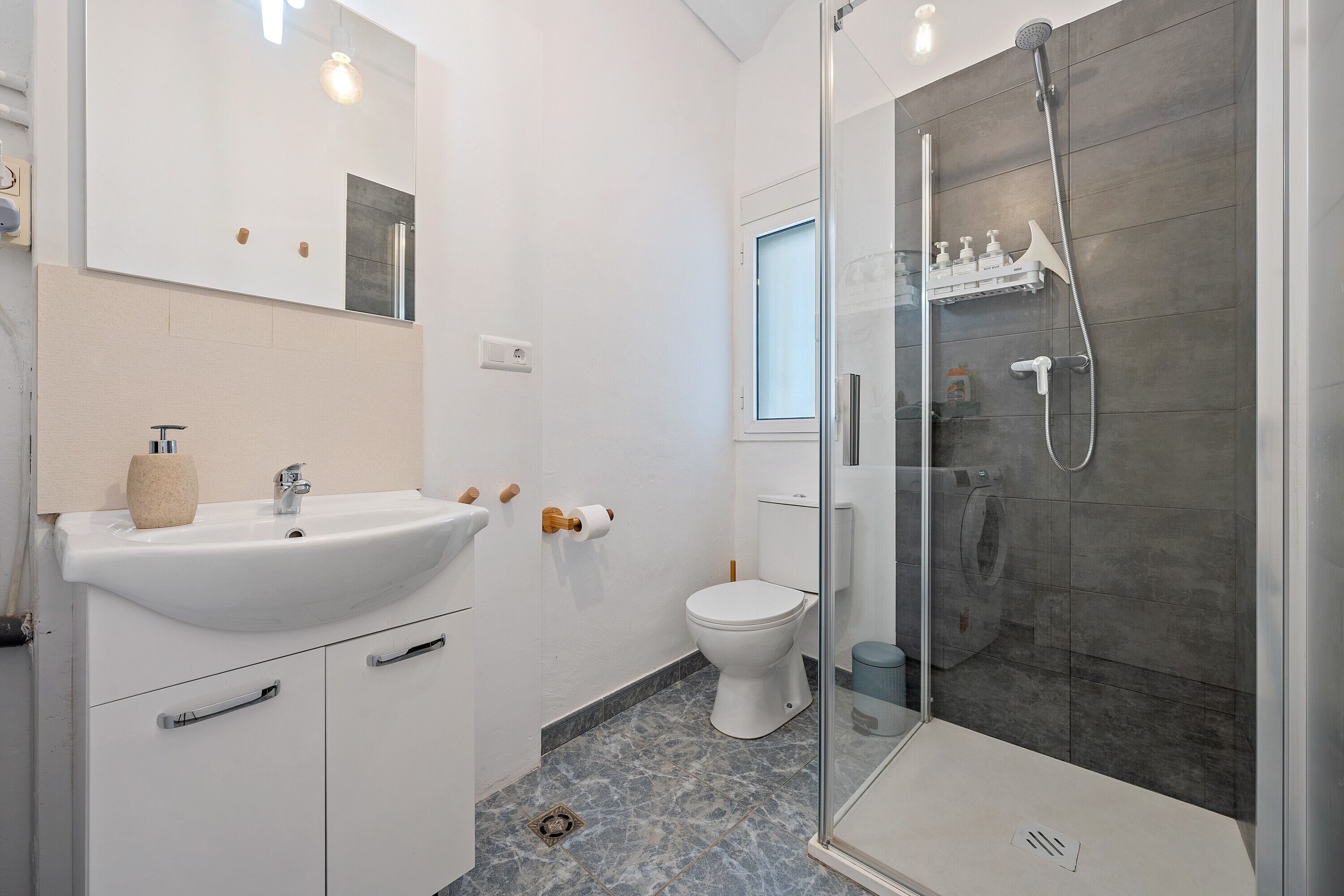 A modern bathroom with a white sink, toilet, and glass-enclosed shower.