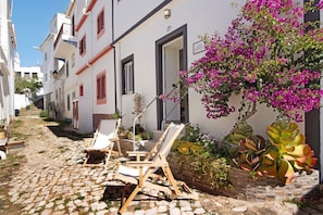 Una estrecha calle adoquinada con edificios blancos, un cartel que dice 'CASA BARROCO' y mesas y sillas para clientes al aire libre.