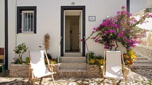 Un edificio con fachada blanca, una puerta con marco negro y una pequeña ventana con barrotes blancos.