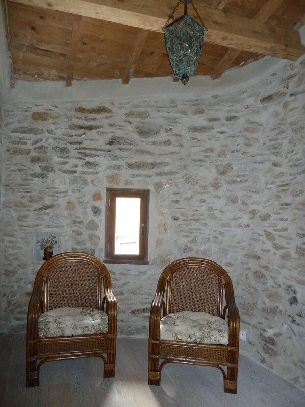 A rustic room with two wicker chairs, a stone wall, a wooden ceiling, and a hanging lantern.