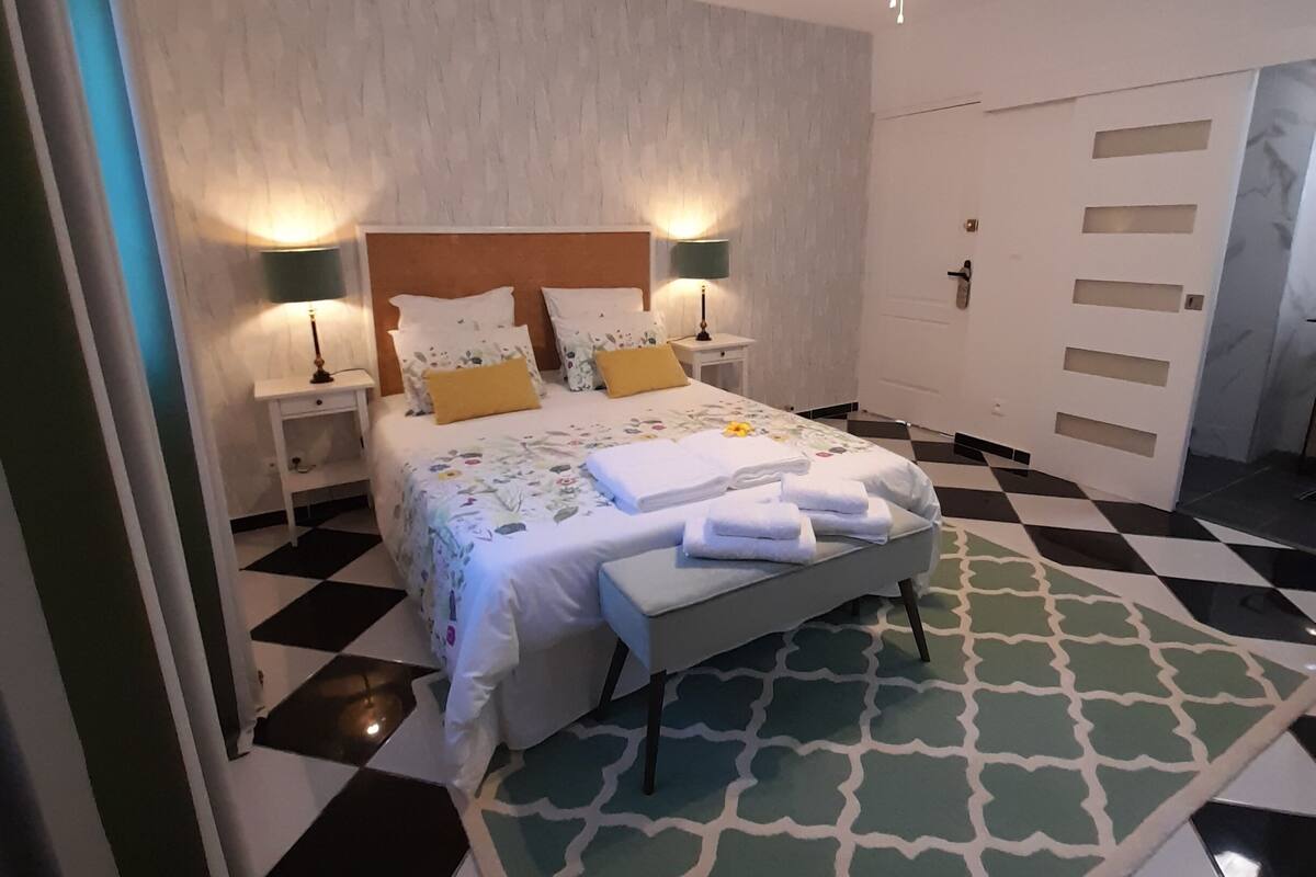 A bedroom with a bed, two bedside tables, a ceiling fan, and a patterned rug.