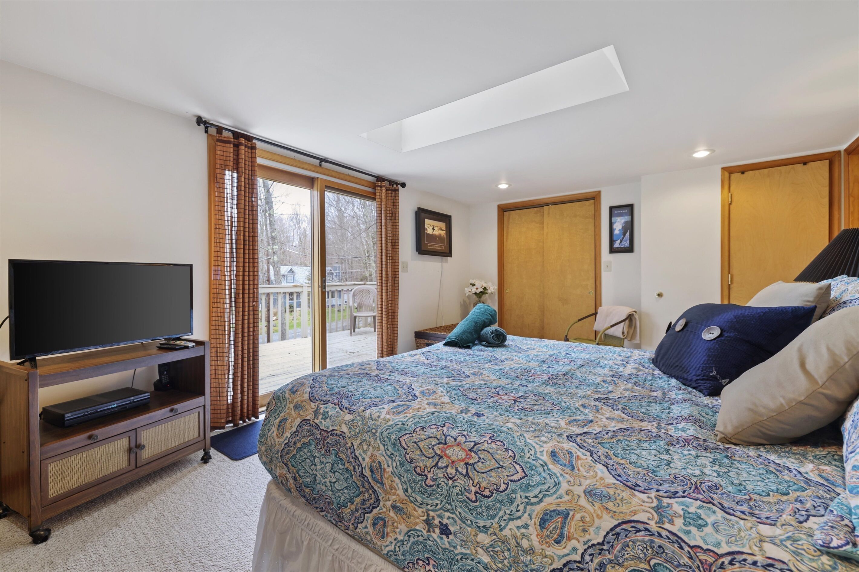 Een slaapkamer met een groot bed, een televisie op een houten dressoir en een glazen schuifdeur naar buiten.
