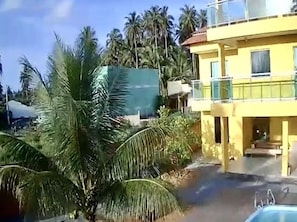 Un edificio amarillo con balcón, rodeado de palmeras y una piscina.