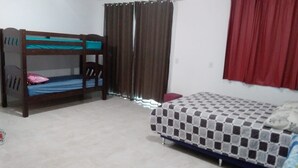 Una habitación con una cama individual, una litera, una silla y una cortina.