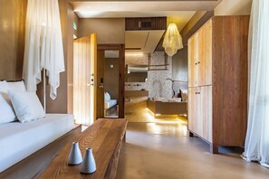 Ein modernes Hotelzimmer mit Holzboden, einem weißen Sofa, einem Holztisch mit Vasen und einem großen Kleiderschrank.