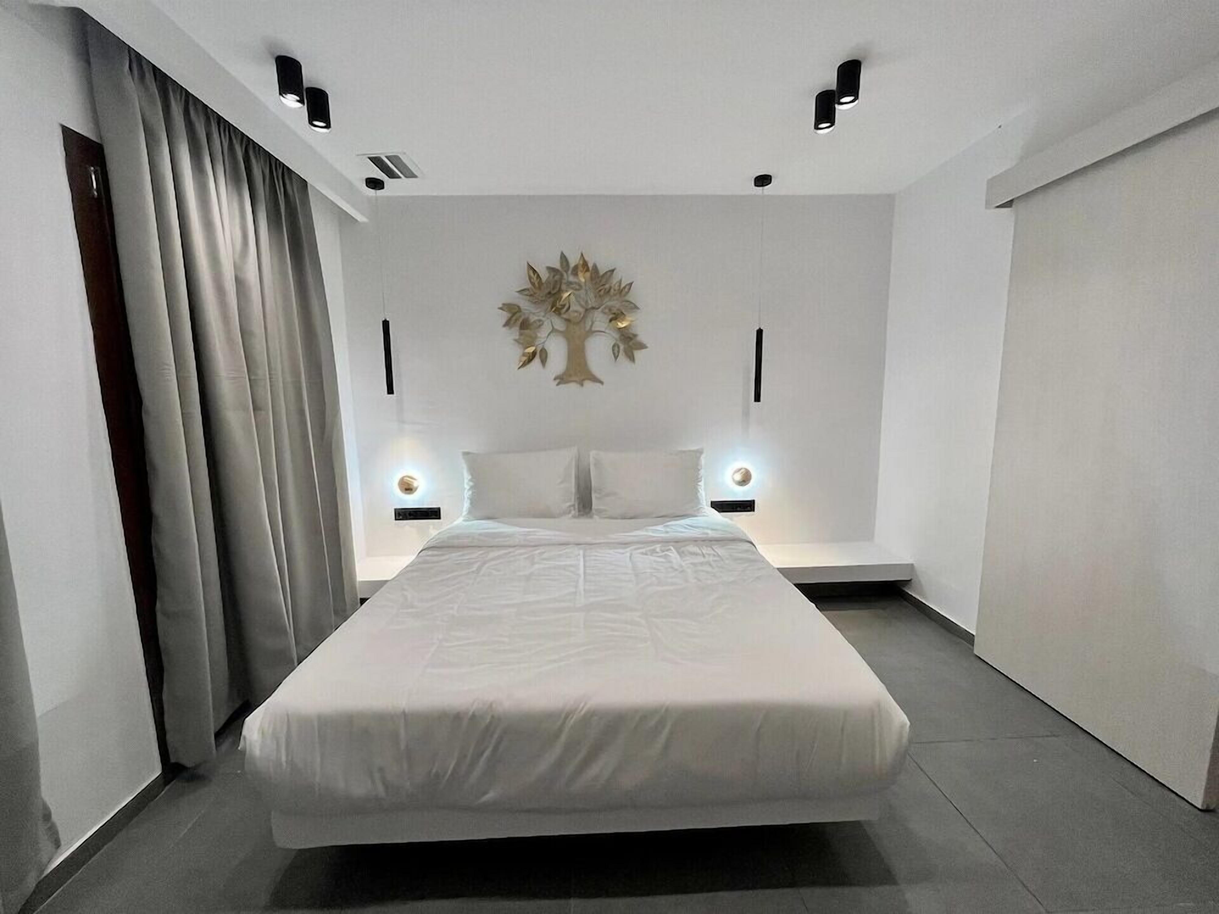 Un dormitorio moderno con una cama grande, dos mesitas de noche, una lámpara de pared y una cortina a la izquierda.