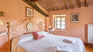 Een slaapkamer met een houten plafond, een bed met witte beddengoed, een nachtkastje met een lamp en een raam met uitzicht.