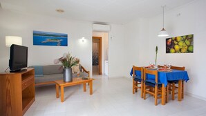 Una sala de estar con televisor, sofá, mesa de centro y zona de comedor con sillas y una mesa.