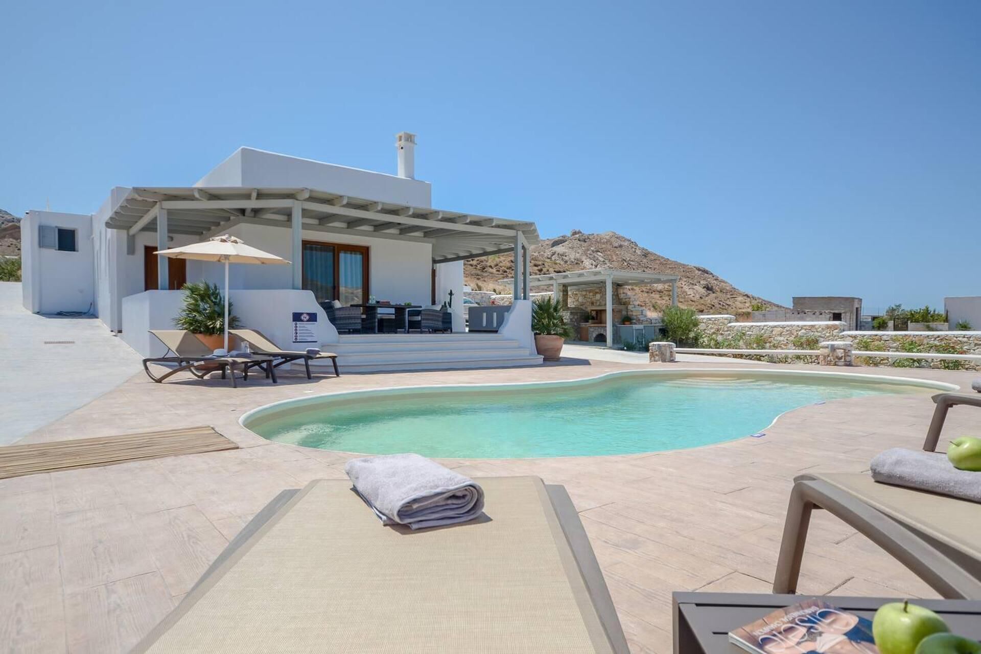 Ein moderner Poolbereich im Freien mit Liegestühlen, einem überdachten Sitzbereich und Blick auf die umliegende Landschaft.