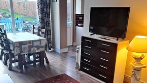 A living room with a dining table, chairs, a TV, a cabinet, and a red patterned rug. - 2-bed Apartment Sleeps 6 With Parking (Kildangan)