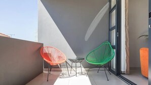 Ein Balkon mit zwei Stühlen, einem kleinen Tisch und einer Schiebeglastür, mit Blick zum Himmel.